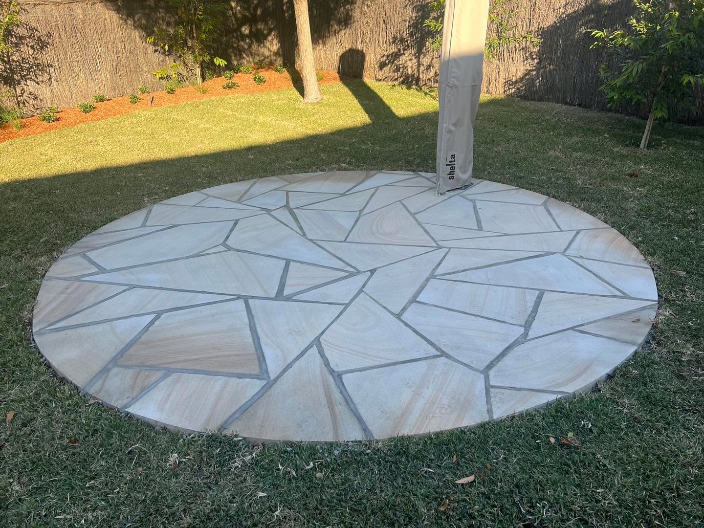 Crazy-paved circular sandstone patio set into lawn