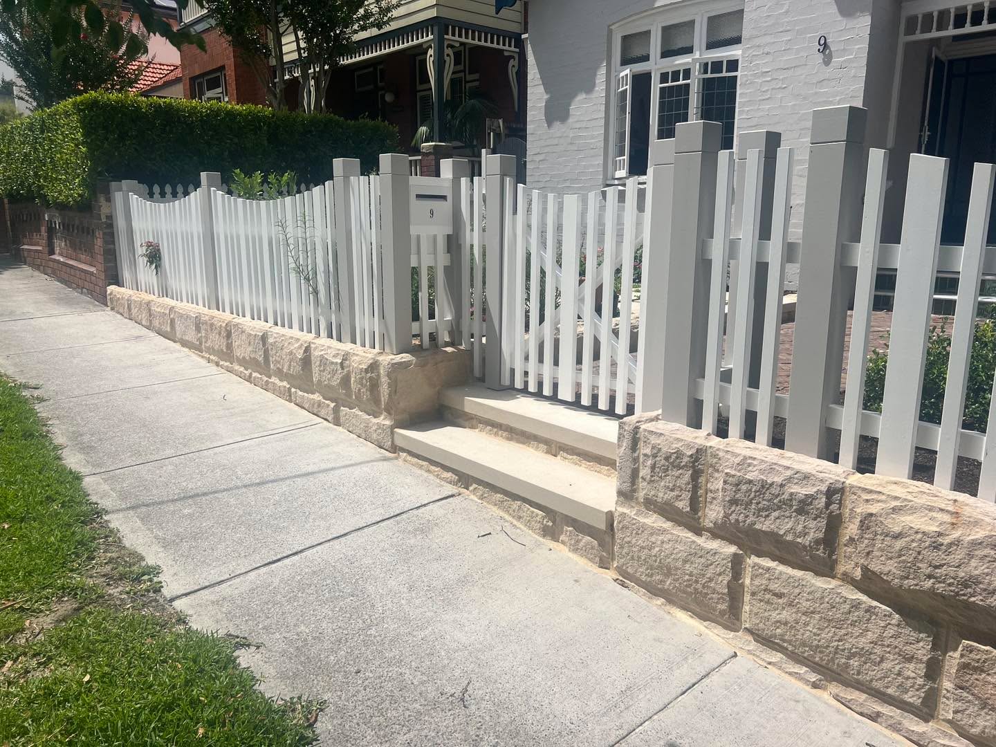 Sandstone block front garden wall with white picket fence in Sydney