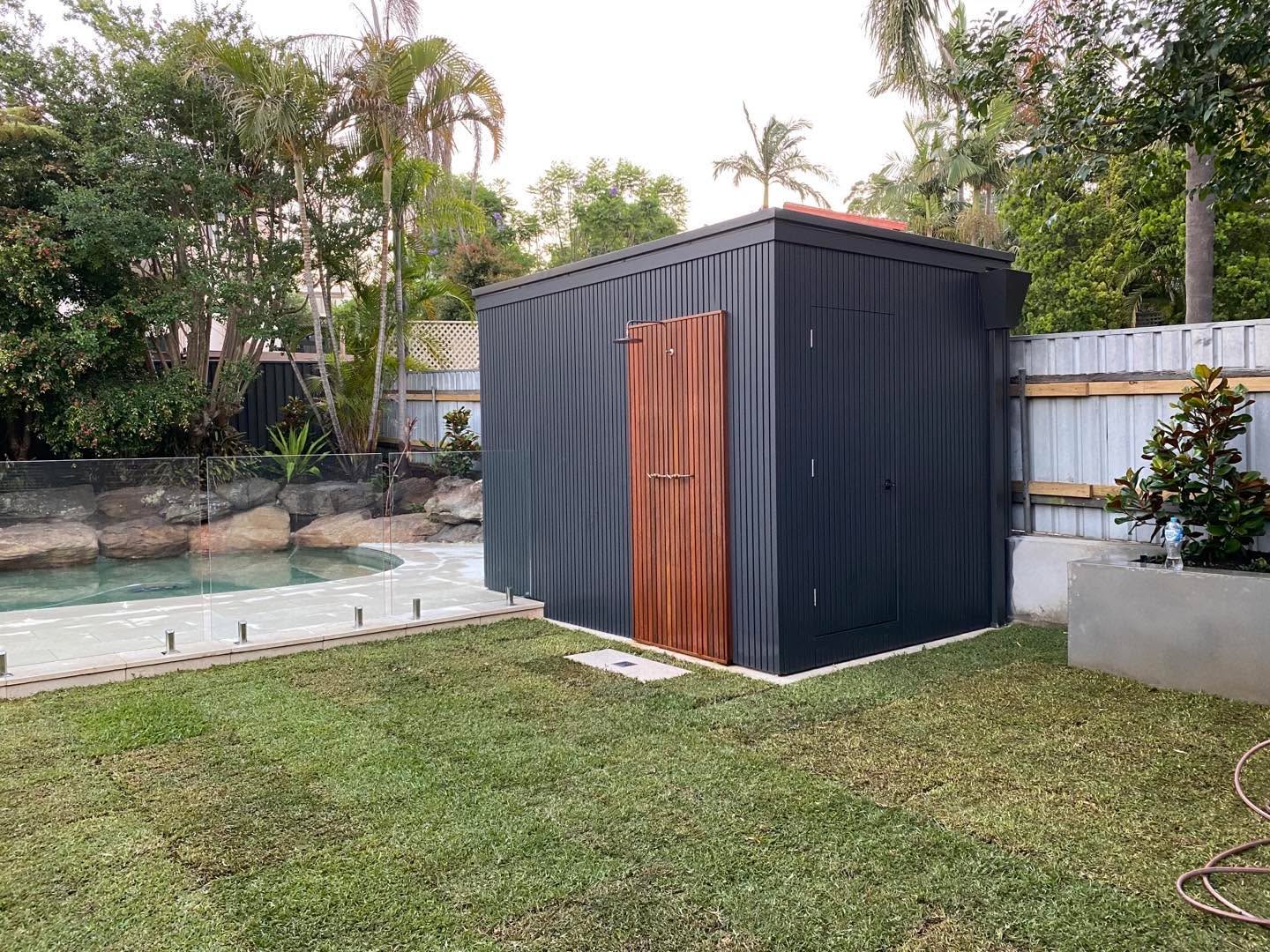 Charcoal-clad garden shed with hardwood door beside a landscaped pool