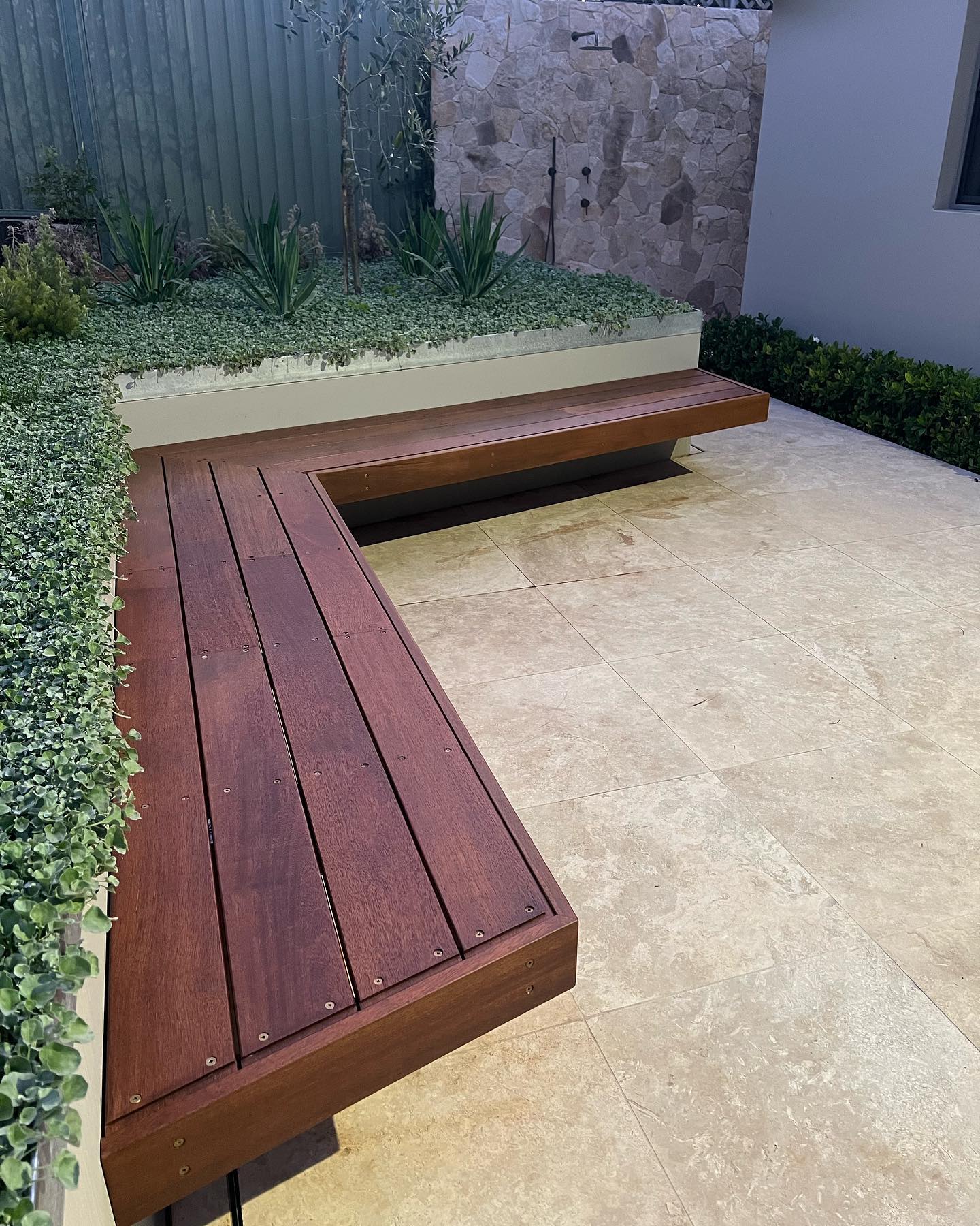 Floating hardwood bench and travertine paving with stone feature wall